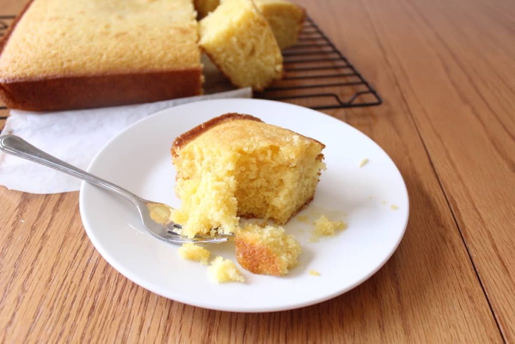 Slice of cornbread on white plate with a bite sitting on a fork