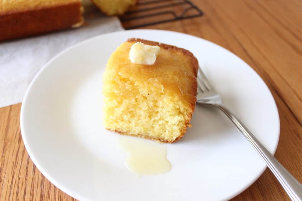 Square of cornbread on white plate with butter and honey
