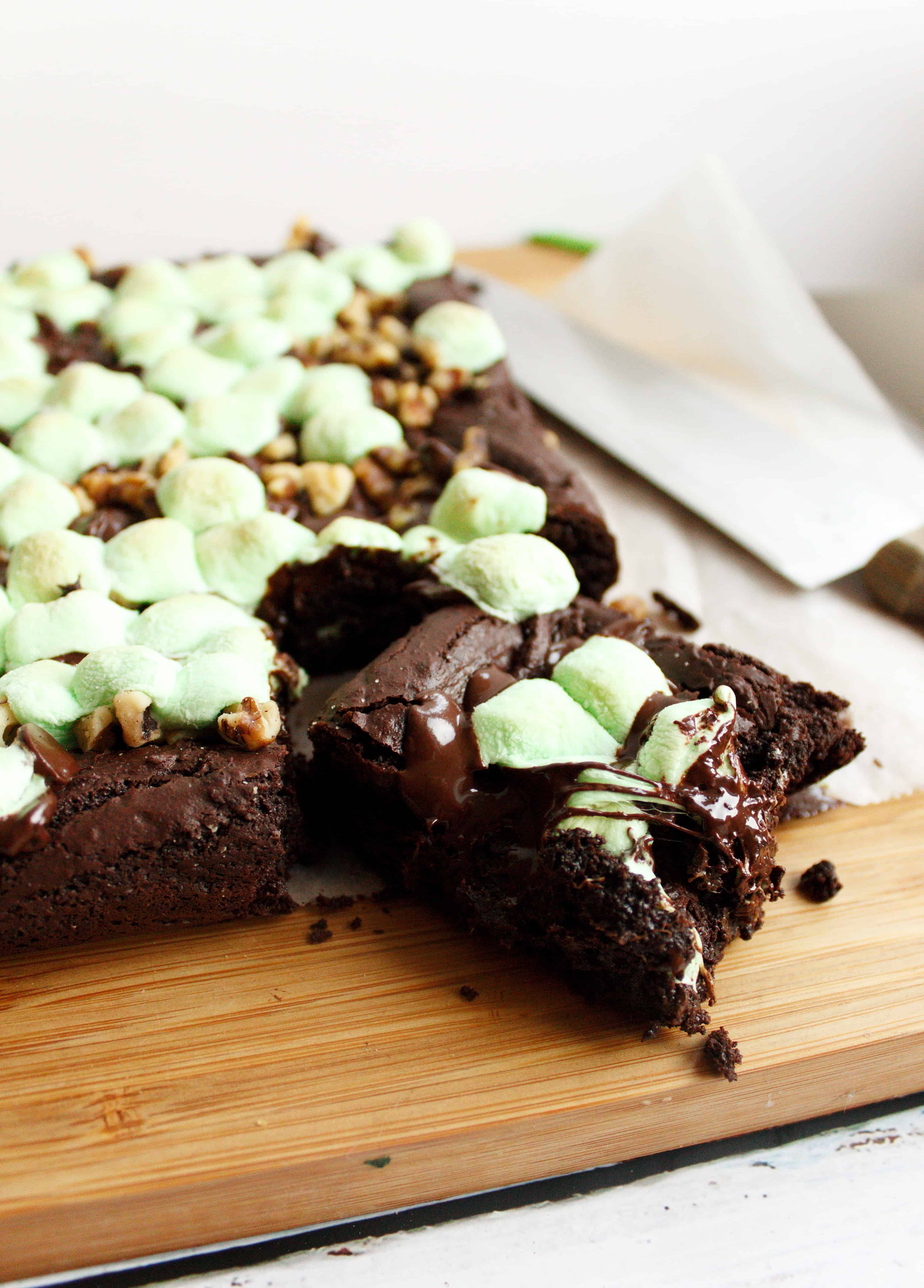 Brownies with marshmallows on top sit on a wooden cutting board
