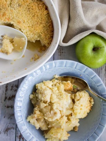 apple crumble in a blue bowl sitting beside a green apple
