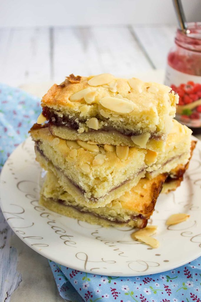 3 almond slices piled on a white plate with a jar of jam on the side