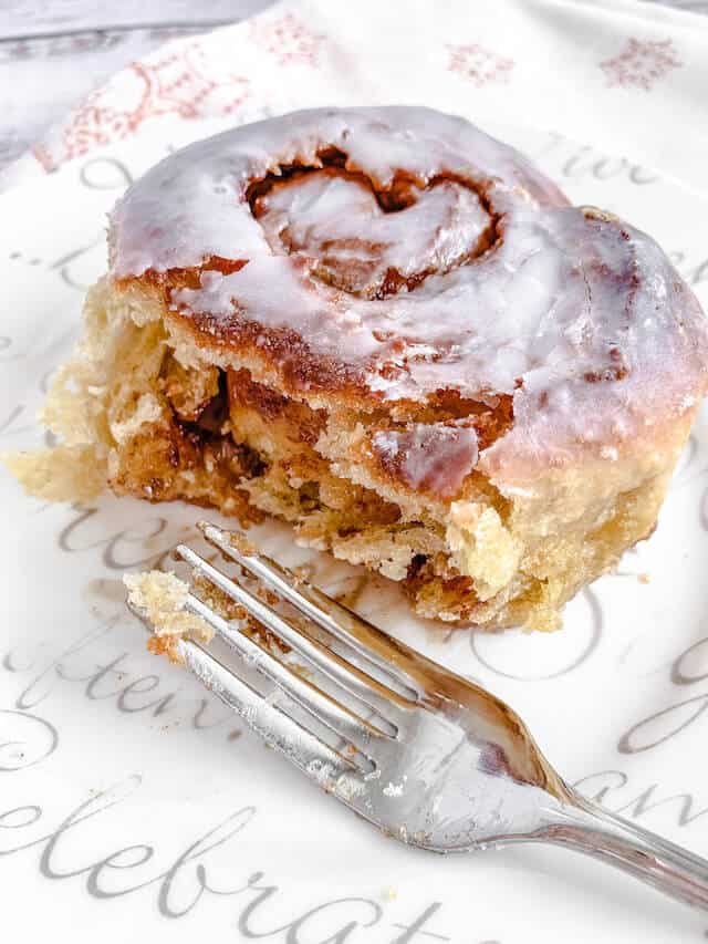 one cinnamon roll on a white plate with a fork