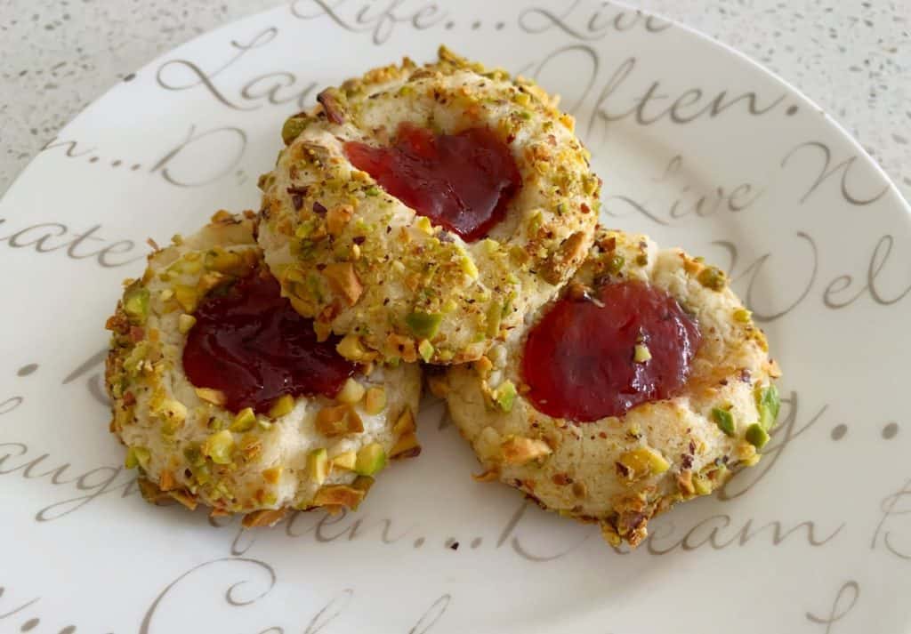 3 pistachio and jam thumbprint cookies on a white plate