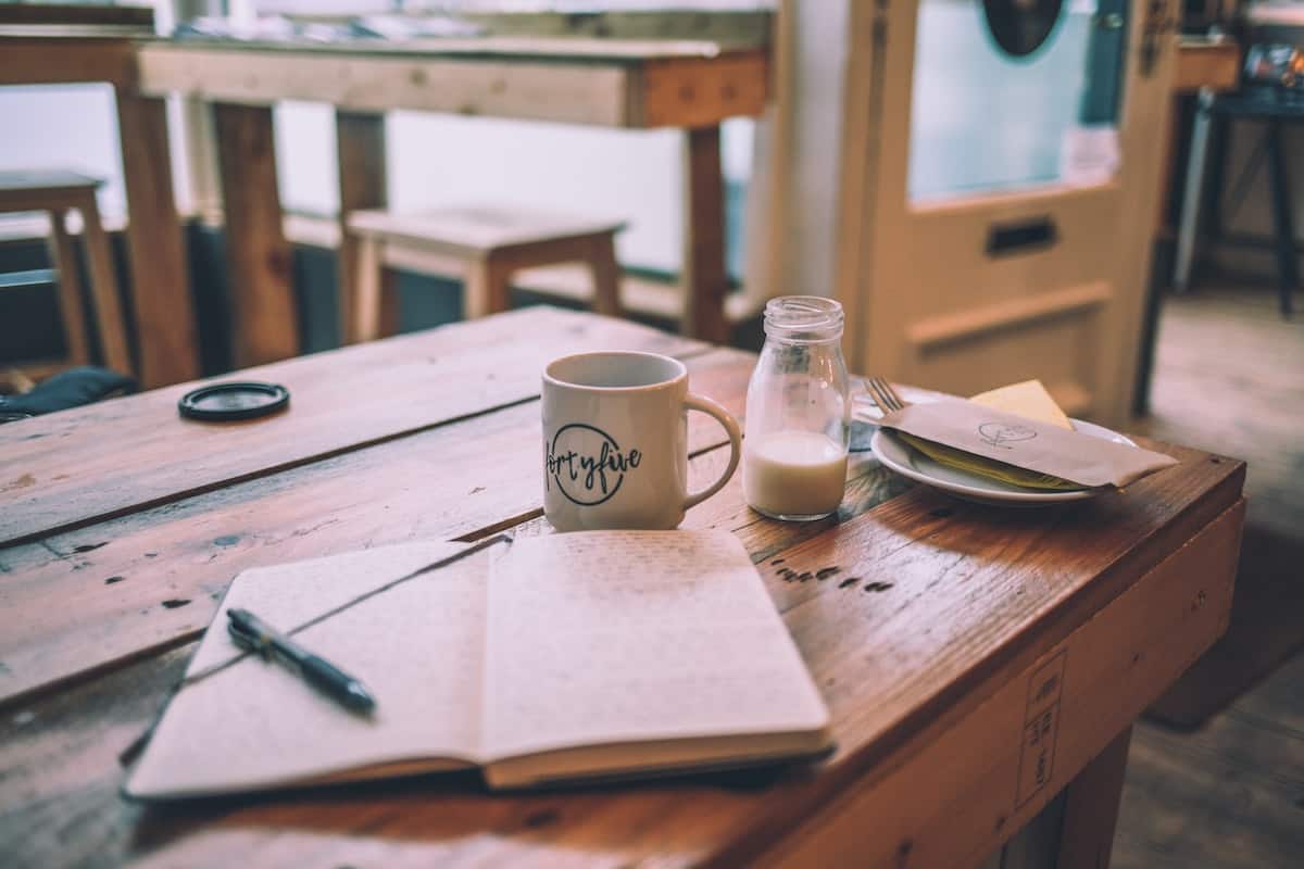 note pad and pen on desk with a mug and glass of milk