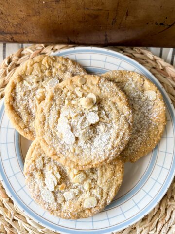 4 almond croissant cookies piled on a white plate.