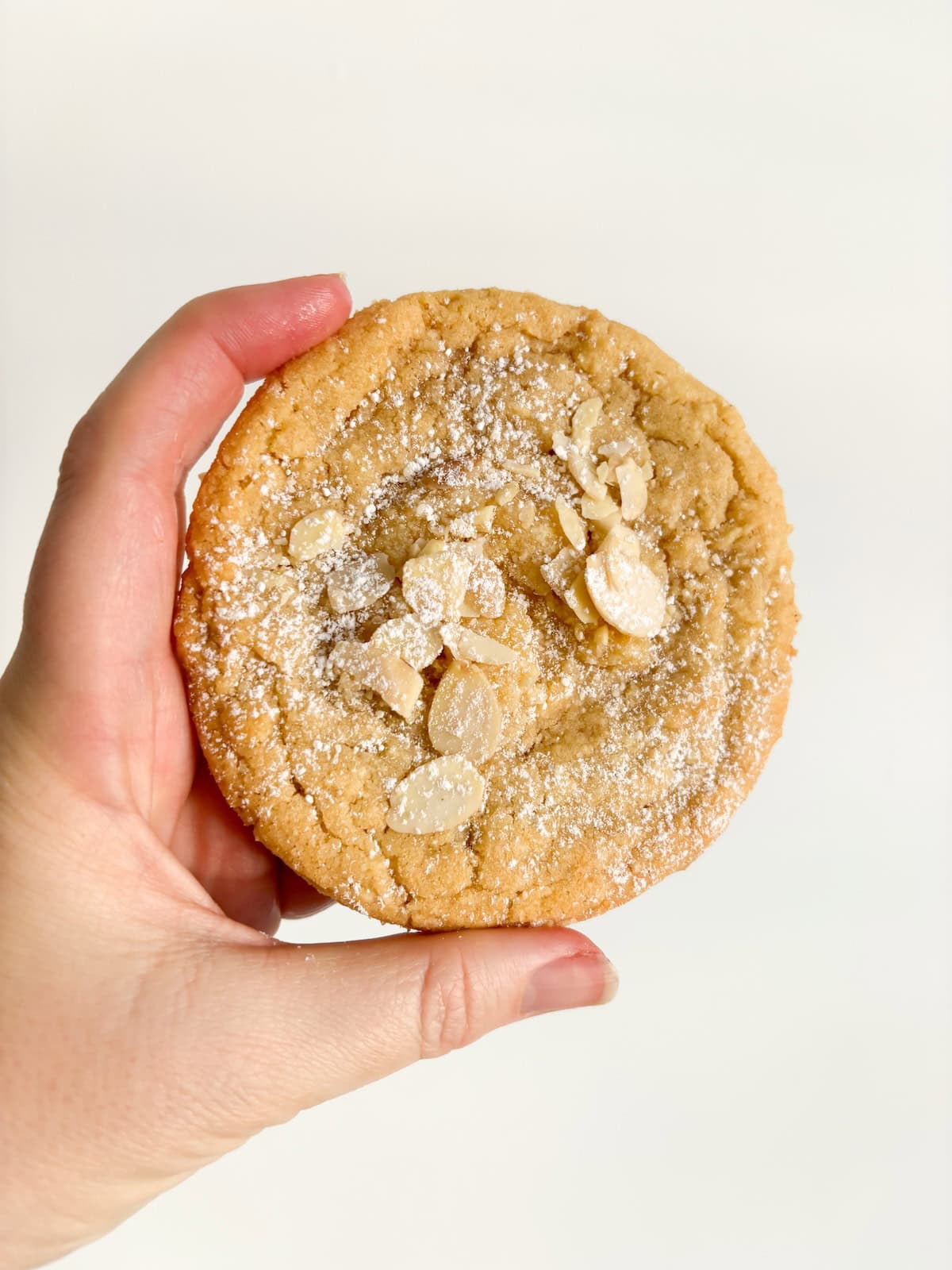 A woman holds up a lemon pie cookie between her finger and thumb.