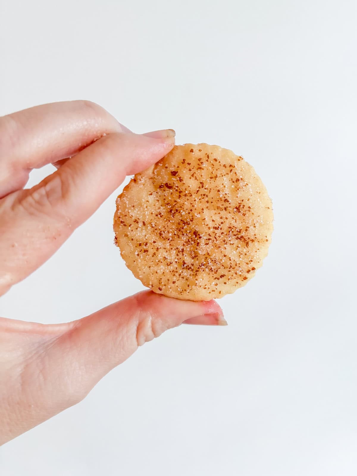 One cinnamon shortbread cookie held between thumb and finger.