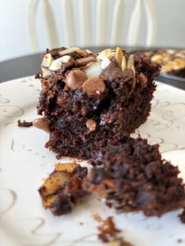 A slice of chocolate cake with chocolate chips and almonds on top.