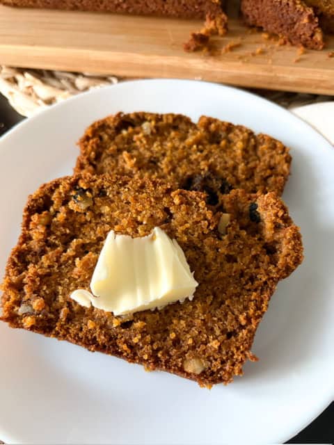 2 slices of pumpkin bread on a white plate with butter on top