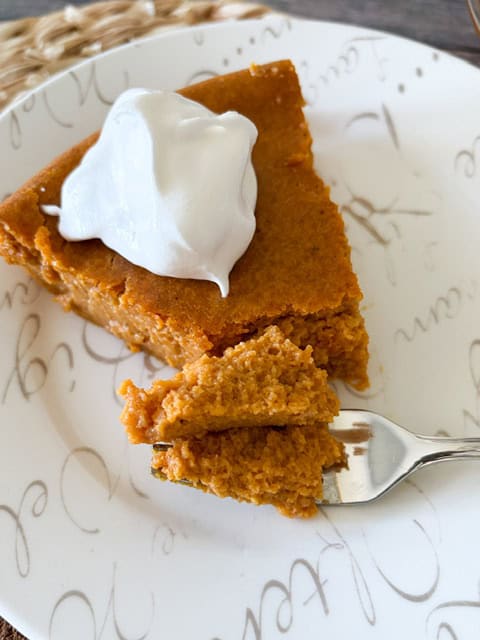 slice of pumpkin pie with whipped cream on top sitting on a white plate.
